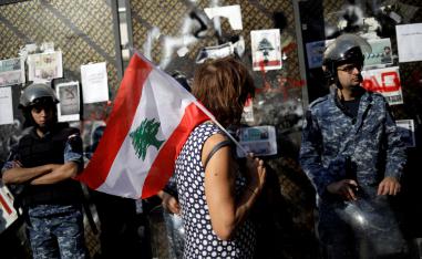 A protester holds a Lebanese flag as she walks in front of police officers