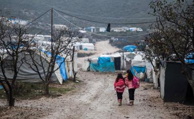 Children walk along a mudpath at a camp for displaced Syrians
