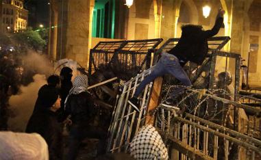 An anti-government protester stands on barriers defense as he throws stones against the riot police in Beirut