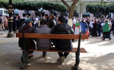 People sit on a bench as protesters demanding a change of the power structure march in Algiers