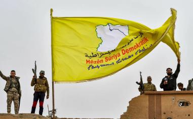 Fighters of the Syrian Democratic Forces (SDF) flash the victory gesture next to their unfurled flag atop a roof at a position in the village of Baghouz 