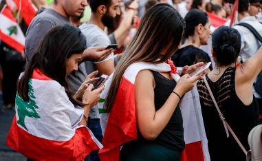 Women draped in the Lebanese national flag use their cell phones during a demonstration against tax increases and official corruption