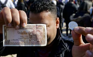 A man shows a Syrian pound in the form of a coin as well as a banknote