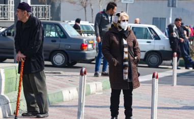 An Iranian woman wearing a protective mask and gloves, stands in a busy street in the capital Tehran