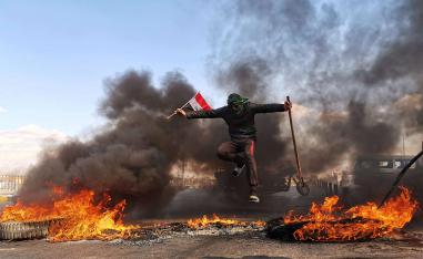 An anti-government protester jumps over burning tires blocking a street during an anti-government protest