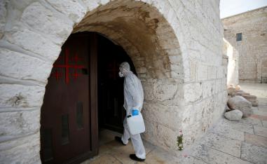 A worker wearing a protective suit arrives to disinfect the Church of the Nativity