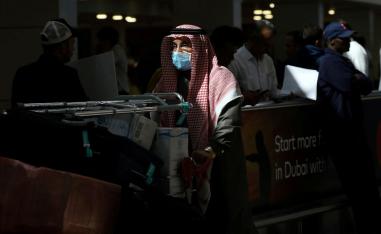 A traveller wears a mask as he pushes a cart with luggage at Dubai International Airport