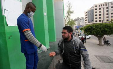 A worker sprays disinfectant on the hands of a Palestinian man at a Post Office in Gaza