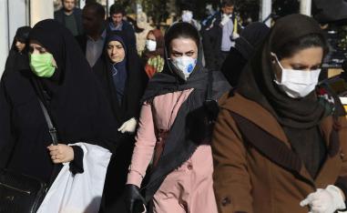 People wearing face masks walk on a sidewalk in downtown Tehran