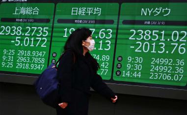 A mask-clad pedestrian passes in front of a quotation board displaying the share price numbers from the Shanghai, Tokyo and New York exchanges, in Tokyo