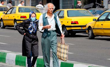 An elderly man and a woman, wearing a protective mask, walk along a street in Tehran