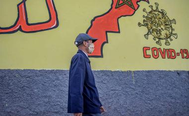 A Moroccan man wearing a protective mask walks past a mural painting of COVID-19