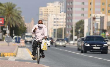 A worker wearing a protective mask bikes on a street in Sharjah