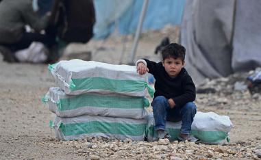 Displaced Syrian boy sits next to humanitarian aid