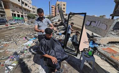 حلاق فلسطيني يعمل أمام ركام دكانه في غزة