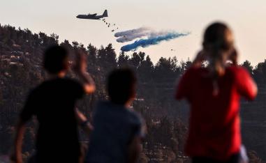 Children look on as an Israeli military plane disperses fire retardant to extinguish a fire near the Israeli kibbutz of Tzuba