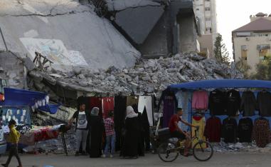 نساء فلسطينيات في سوق أمام مبنى مدمر في غزة