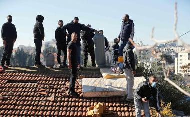 Palestinian men hold a gas tank on the roof of a house as Israeli police try to evict a family from the same building