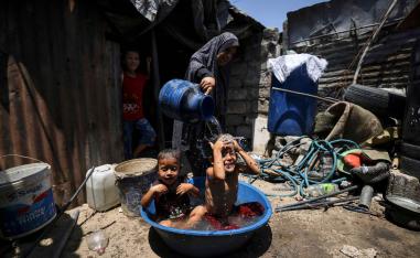 ام فلسطينية تبرد أولادها بالماء في موجة الحر التي تضرب غزة