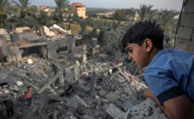 A child watches from a window as people sift through the rubble of a building hit in an Israeli air strike in Biet Hanoun
