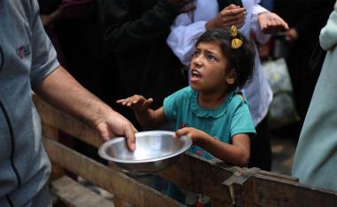 A Palestinian girl holds an empty pan at a hot meal distribution point in Nuseirat in the central Gaza Strip