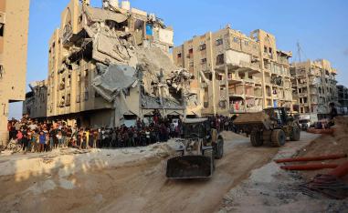 People watch as Palestinians use excavators to dig deep into the ground reportedly searching for bodies in Khan Yunis 