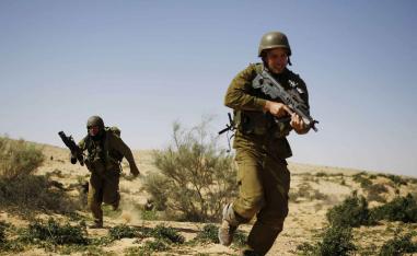 Israeli reserve soldiers run with their weapons during a drill at a military zone near Kibbutz Revivim in southern Israel. 