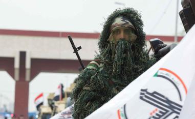A member of Iraq’s Popular Mobilisation Forces (PMF) rides in a military vehicle next to a flag during a parade in Baghdad, December 10, 2025. 