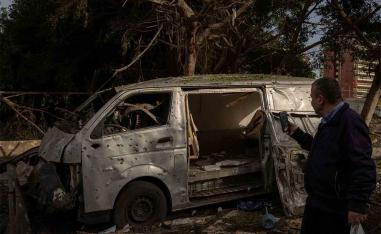 A man takes a photo of a damaged car following an Israeli strike on Beirut