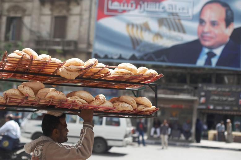 عامل يحمل خبزا يمر بالقرب من ملصق للرئيس المصري