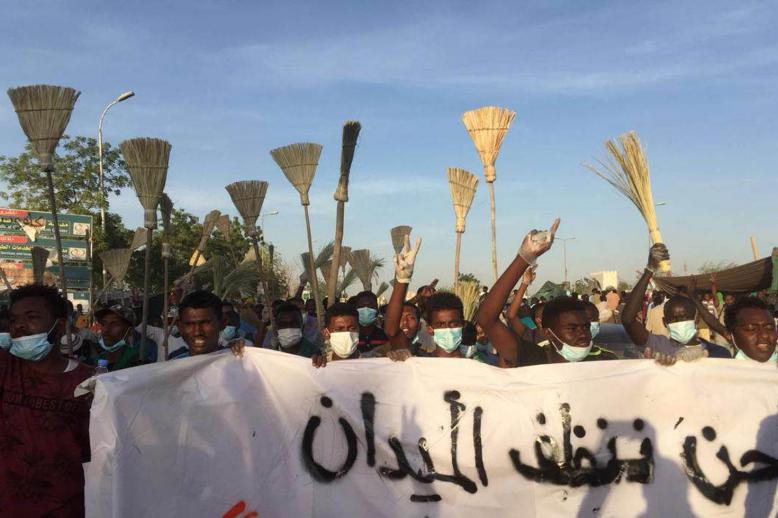 سودانيون يتظاهرون رافعين المكانس أمام مبنى قيادة الجيش