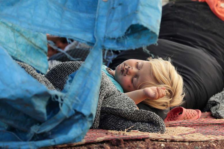 A displaced Syrian child sleeps on a mat laid out on the floor in an olive grove in the town of Atmeh, Syria