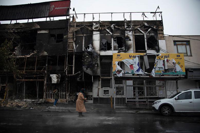 People walk past buildings which burned during protests in the city of Karaj, west of the capital Tehran