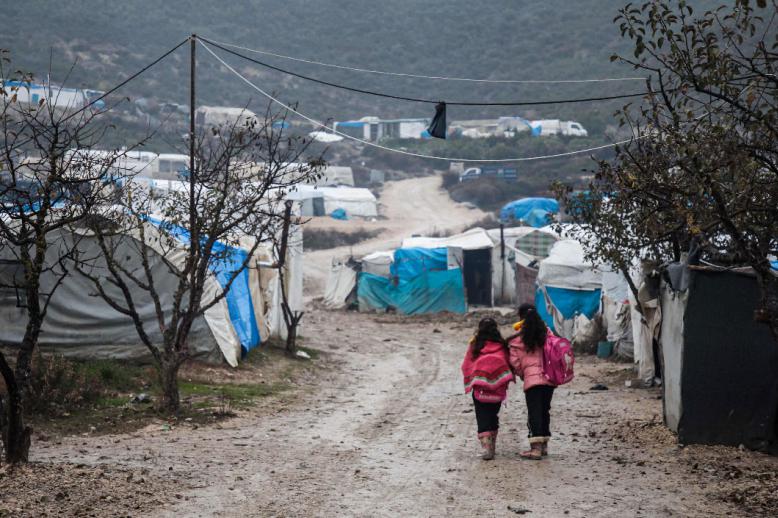 Children walk along a mudpath at a camp for displaced Syrians