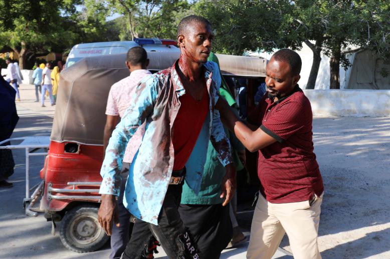 A man assists a civilian injured at the scene of a car bomb explosion at a checkpoint in Mogadishu