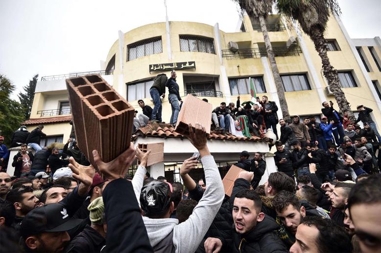Algerian demonstrators carry bricks to build a wall at the entrance of the daira (sub-prefecture) of Tizi-Ouzou