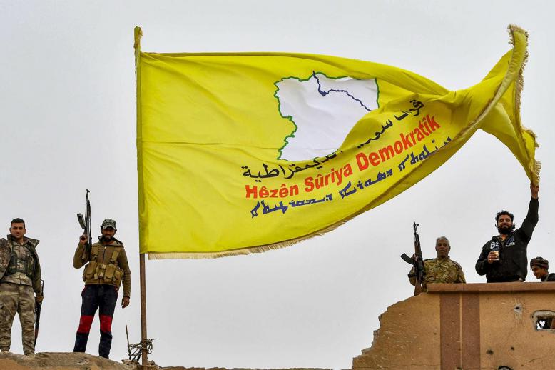 Fighters of the Syrian Democratic Forces (SDF) flash the victory gesture next to their unfurled flag atop a roof at a position in the village of Baghouz 