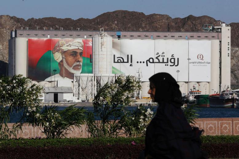 عمانية تمر بالقرب من لوحة تغطي مبنى حكومي في مسقط