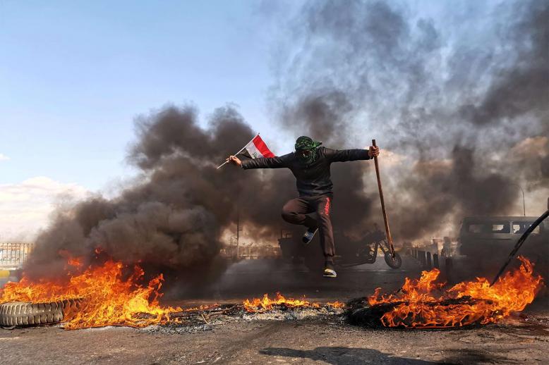 An anti-government protester jumps over burning tires blocking a street during an anti-government protest