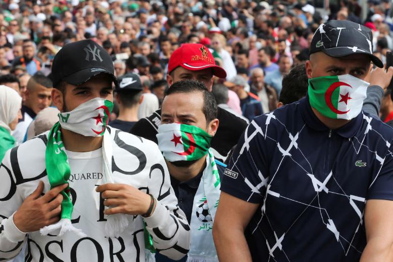 Demonstrators cover their faces with national flags during an anti-government protest in Algiers