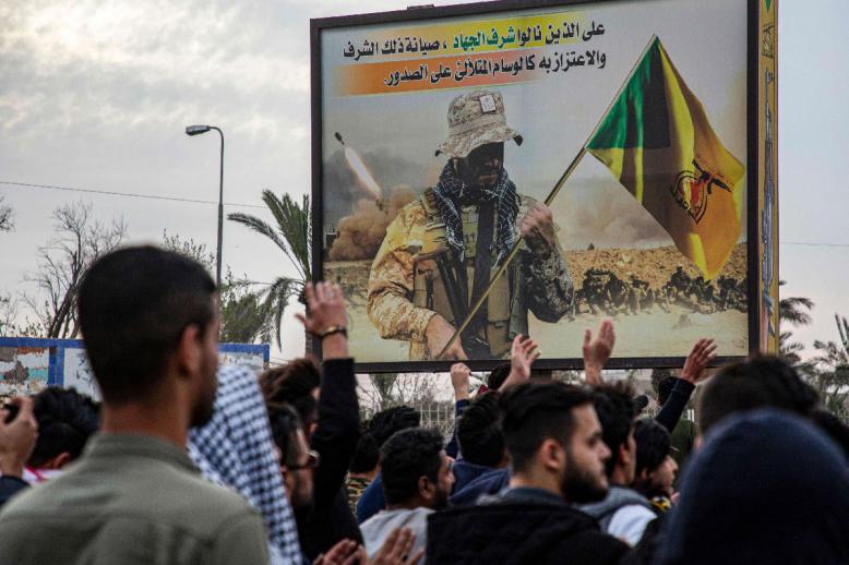 Protesters chant slogans as they walk past a Kata'ib Hezbollah's billboard during an anti-government demonstration in Basra