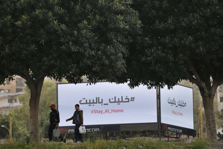 جلان يمران أمام لوحات إعلانية تعرض رسالة تحث المواطنين على البقاء في منازلهم في بيروت
