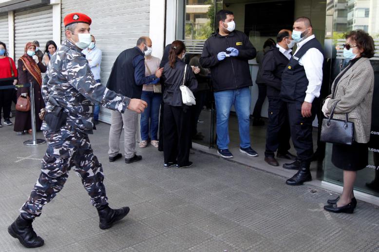 A Lebanese police officer walks near a crowd formed outside a money transfer office
