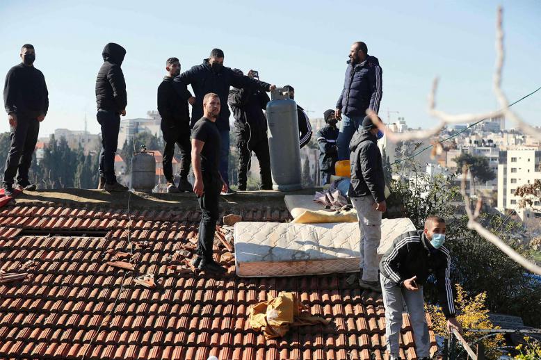 Palestinian men hold a gas tank on the roof of a house as Israeli police try to evict a family from the same building