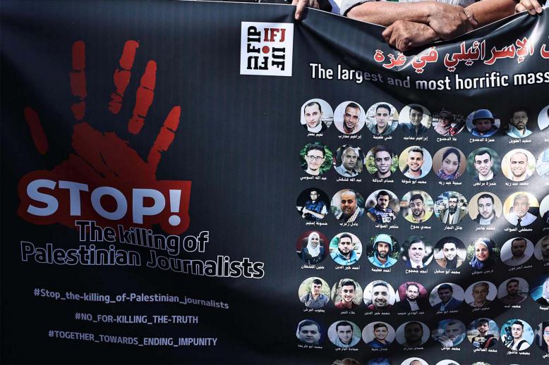Protesters carry a banner bearing pictures of slain Palestinian journalists during a rally to condemn their killing