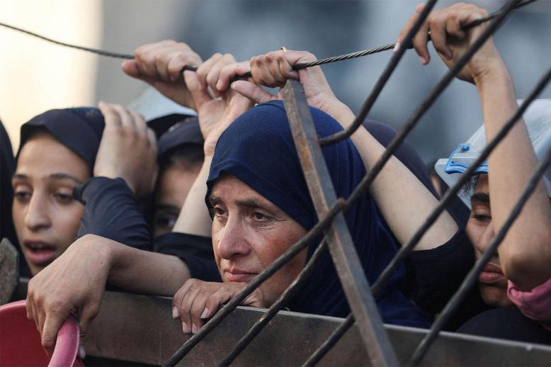 Palestinians look on as they wait to receive food from a charity kitchen amid a hunger crisis in Gaza City