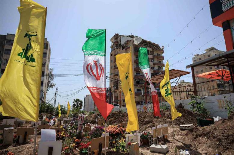 Hezbollah and Iranian flags flutter at a temporary graveyard by a damaged building in Tyre, south Lebanon