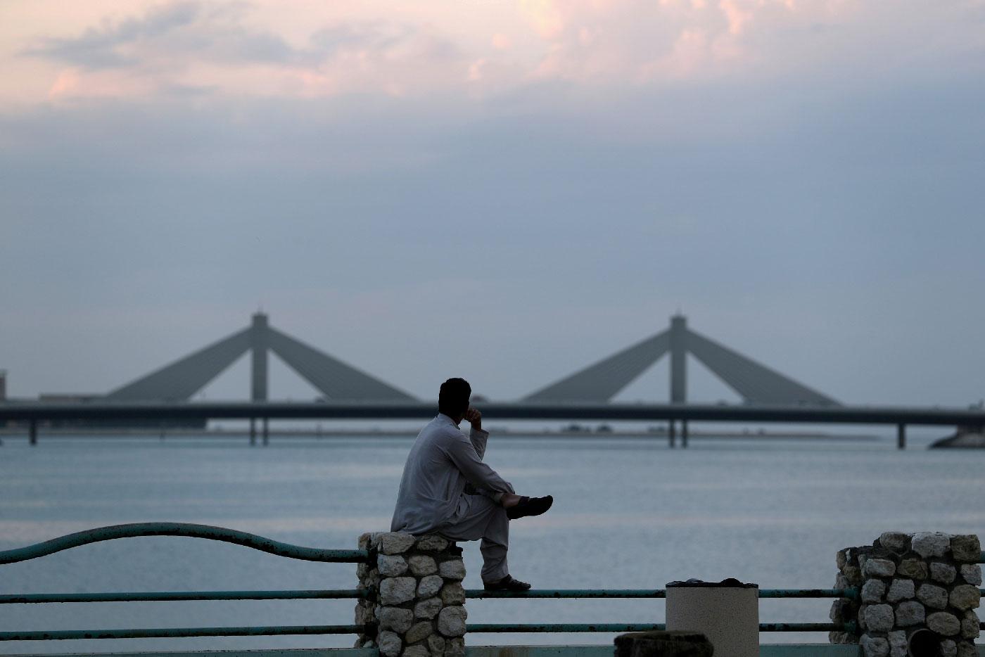 A man sits and looks towards the Sheikh Isa Causeway, linking Diplomatic Area to Muharraq, during the early evening hours in Manama, Bahrain, November 11, 2018.