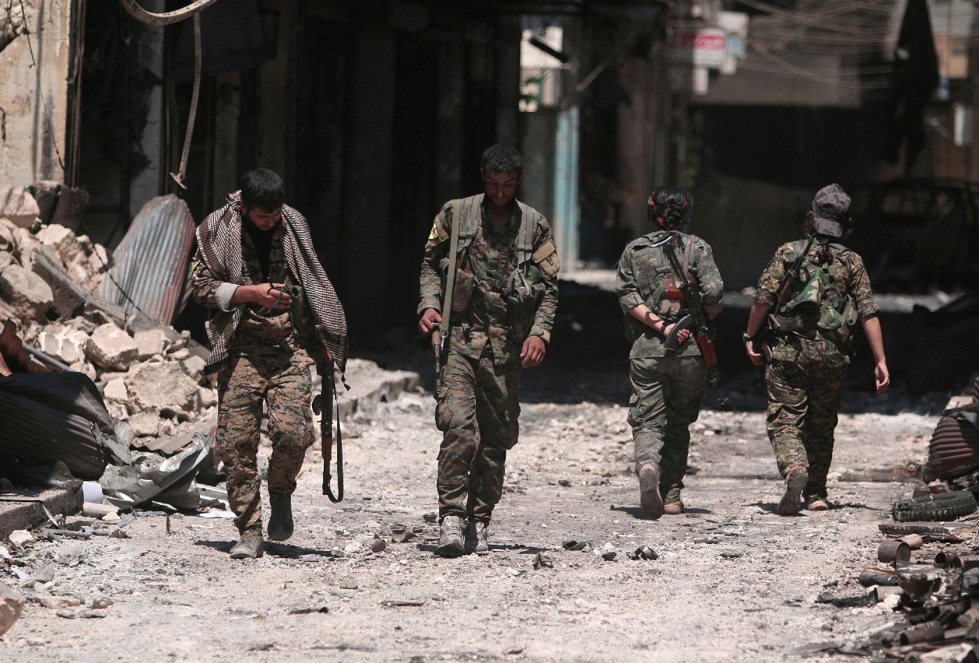 Syria Democratic Forces (SDF) fighters walk on the rubble of damaged shops and buildings in the city of Manbij, in Aleppo Governorate, Syria, August 10, 2016. 