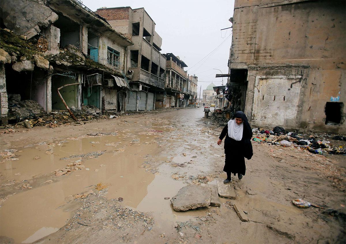 A woman walks next to damaged shops in the Old City of Mosul